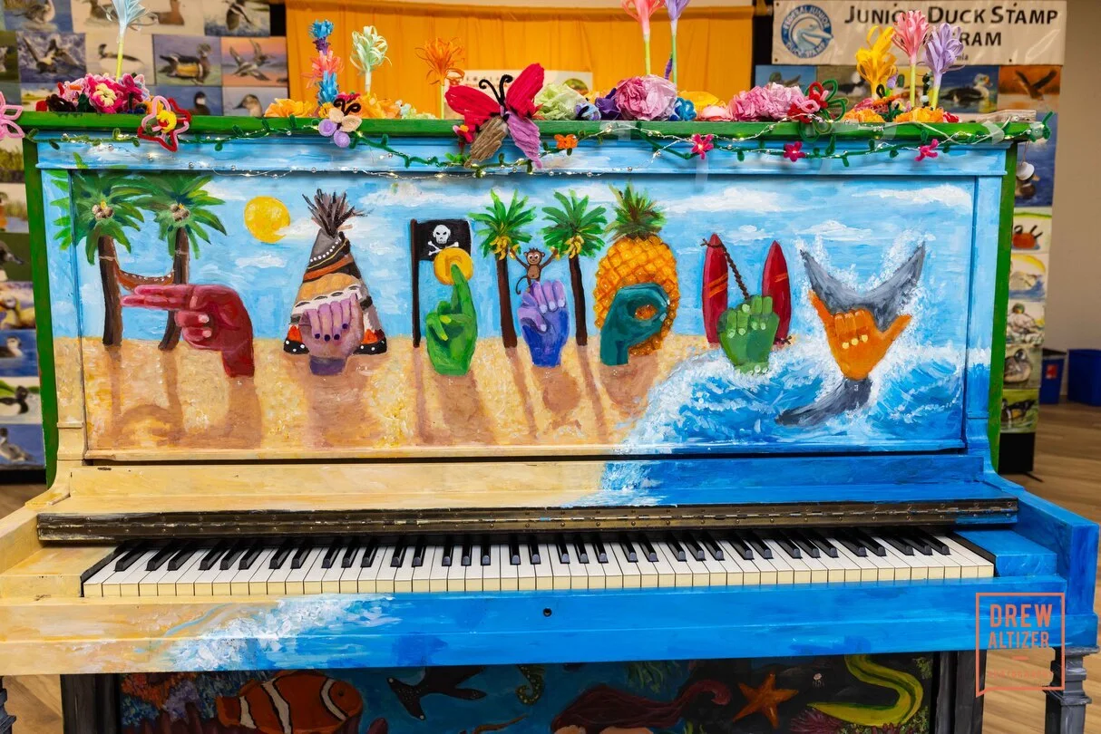 A piano painted with a beach scene and a row of painted hands